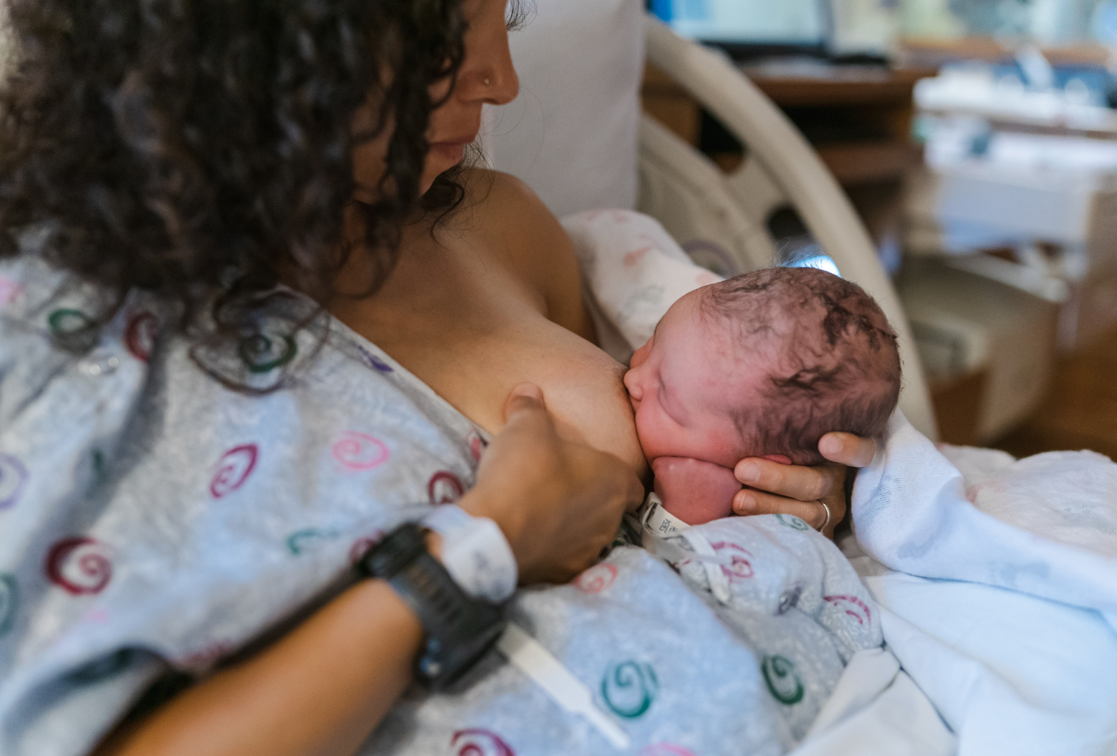 Mother in hospital gown breastfeeding newborn skin-to-skin (photo)