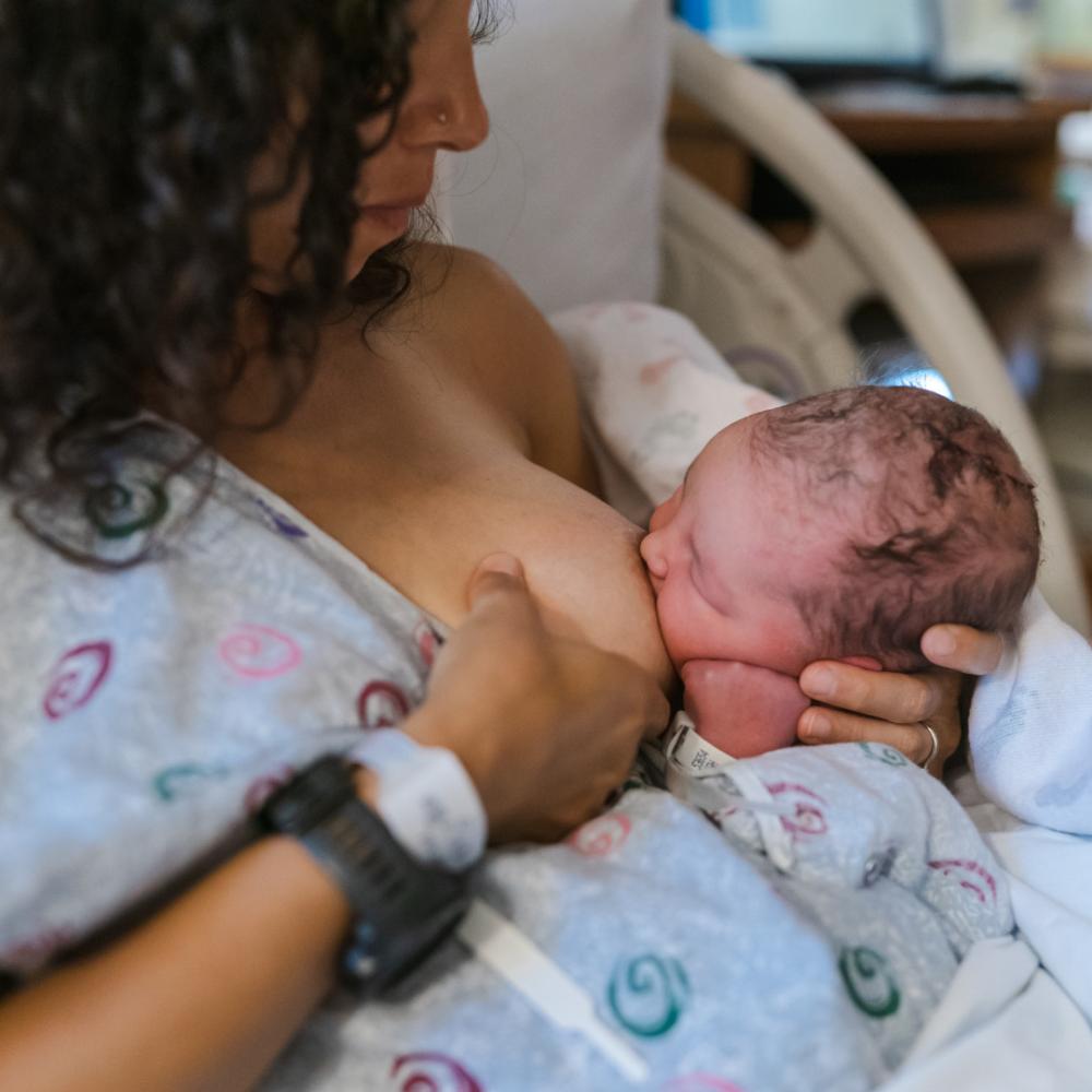 Mother in hospital gown breastfeeding newborn skin-to-skin (photo)