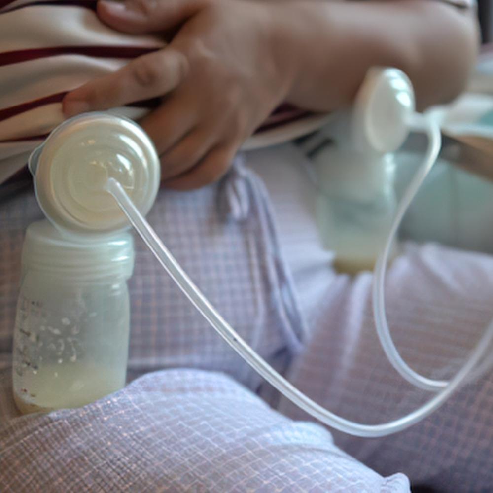 Person using electric double breast pump, milk-filled bottles resting on lap