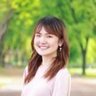 Portrait photo of a smiling young woman with shoulder-length brown hair in a green park