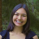Smiling young woman headshot, black top, green foliage background (photo)